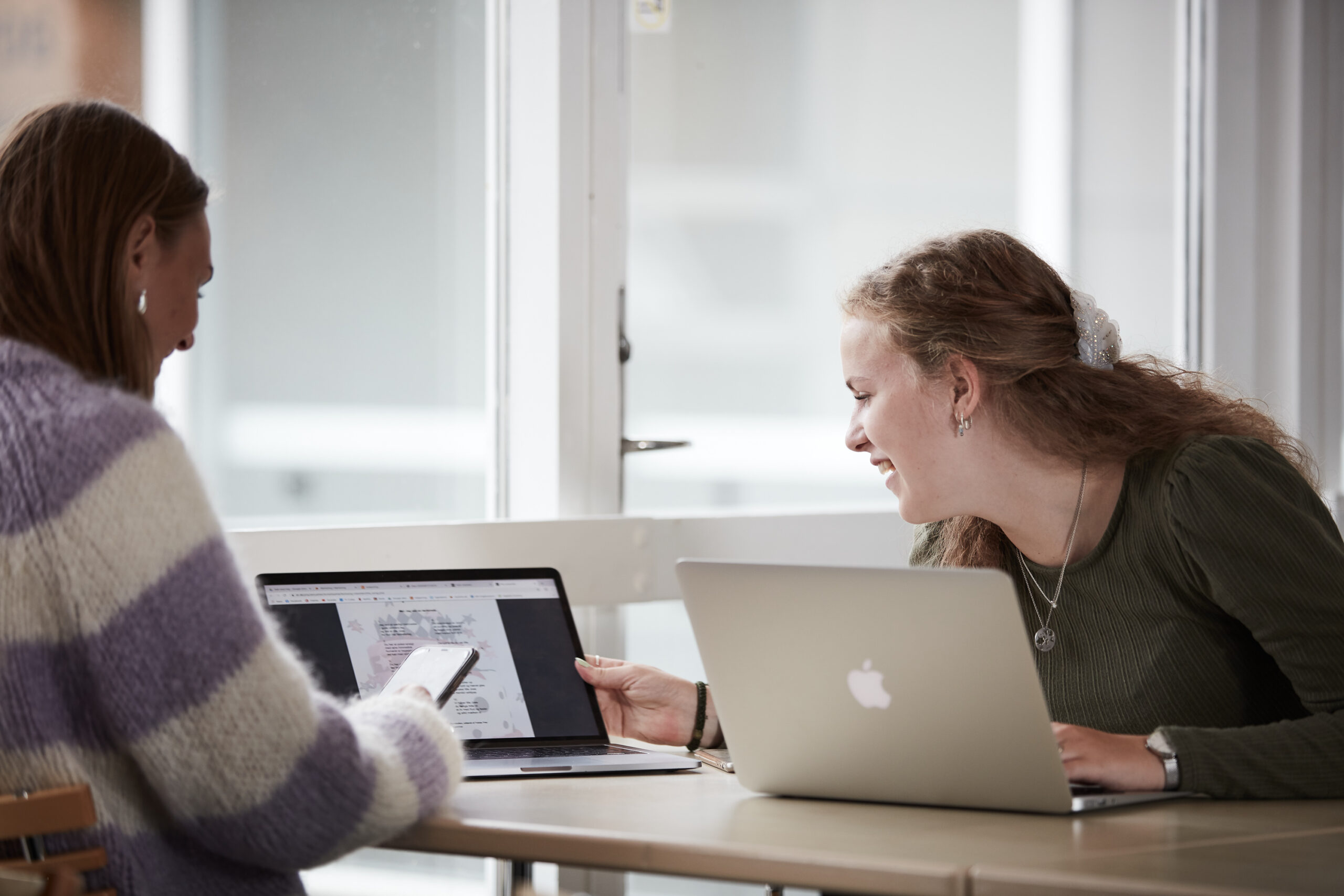 2 smilende piger der studerer og laver gruppearbejde
